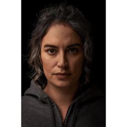 Close-up portrait of a woman with dark hair and a grey hoodie against a black background by Nick Eagle