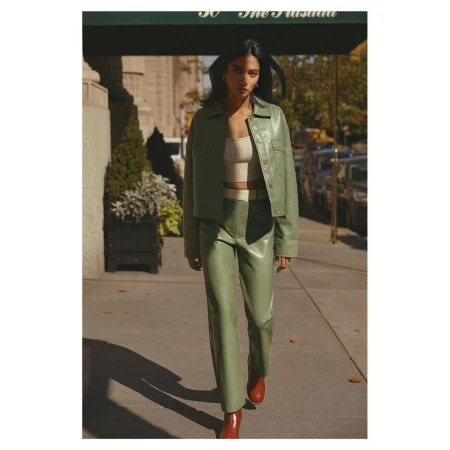 Woman in light green leather jacket and pants poses on urban sidewalk near building, showcasing modern fashion with a neutral top and tan boots.