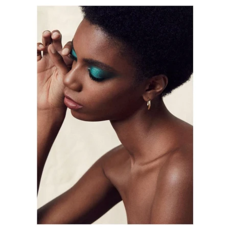 Close-up beauty shot of a young Black woman with blue eye shadow, gold hoop earrings and natural short hairstyle on neutral background.