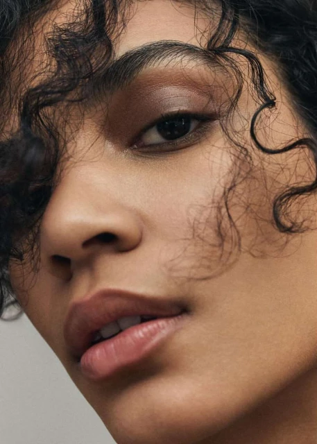Close-up portrait of a woman with curly dark hair and brown eye shadow, highlighting her face and soft skin tone.