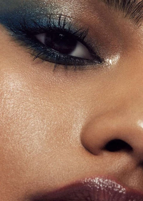 Close-up shot of a person's face with blue eyeshadow and glossy lips, capturing makeup details and skin texture.