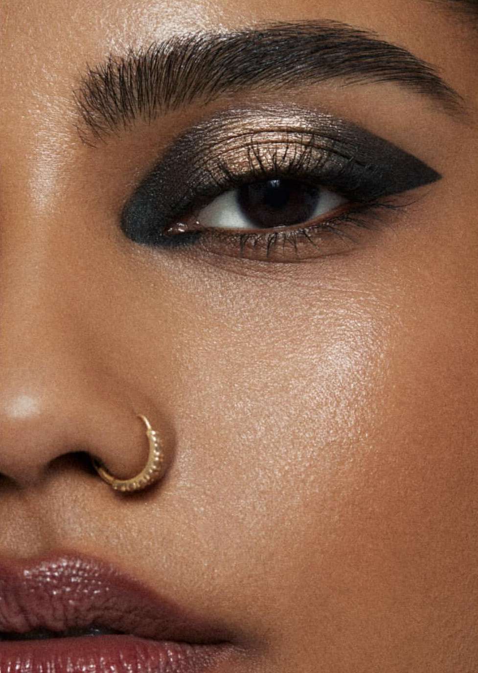 Close-up of a woman's face with striking dark eyeshadow and winged eyeliner, emphasizing beauty and cosmetic artistry in a studio setting.