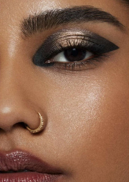 Close-up of a woman's face with striking dark eyeshadow and winged eyeliner, emphasizing beauty and cosmetic artistry in a studio setting.