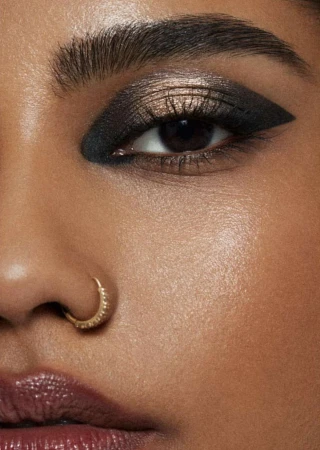Close-up of a woman's face with striking dark eyeshadow and winged eyeliner, emphasizing beauty and cosmetic artistry in a studio setting.