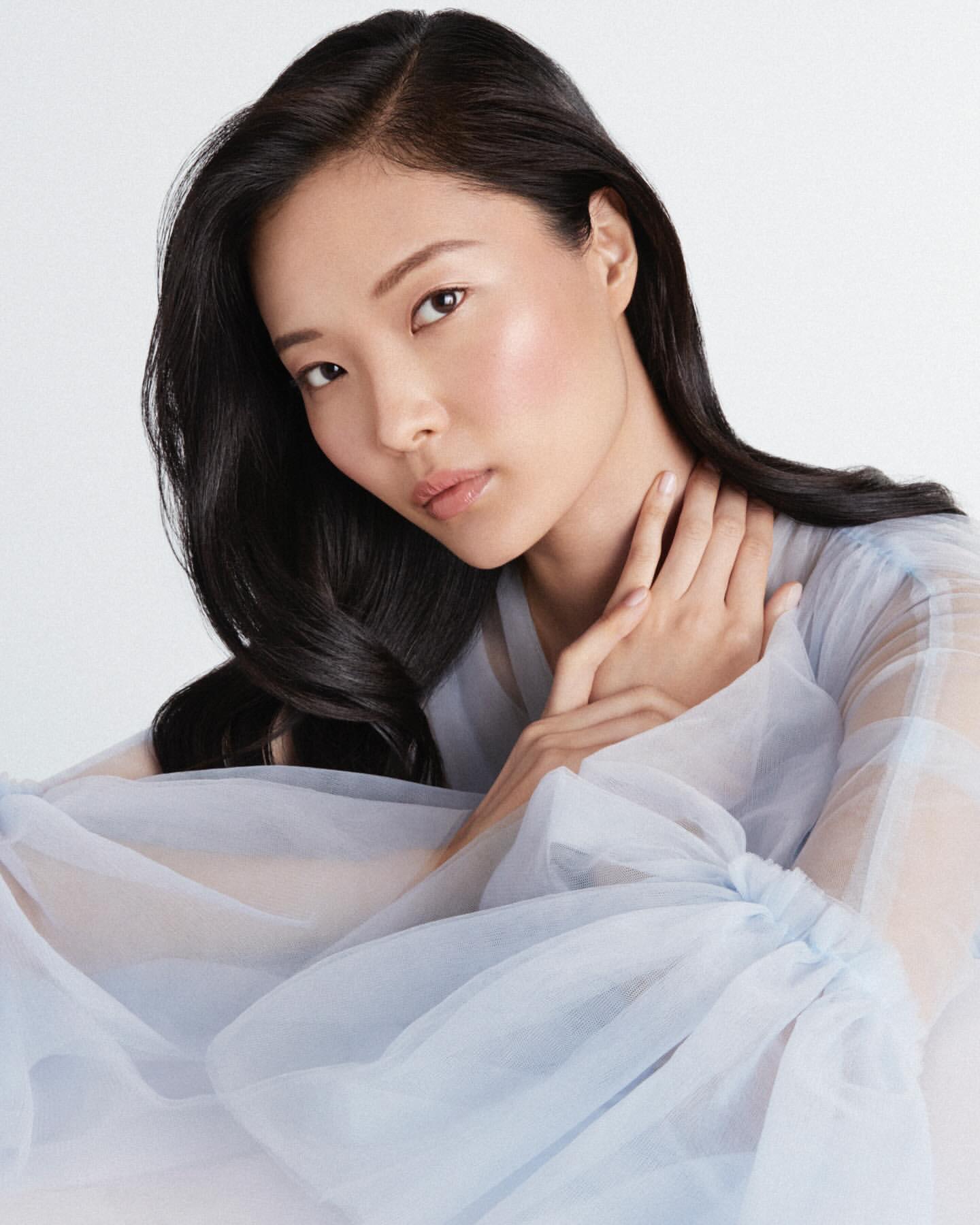Portrait of an East Asian woman wearing a pale blue sheer tulle top against a clean white studio background