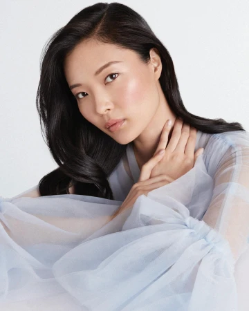 Portrait of an East Asian woman wearing a pale blue sheer tulle top against a clean white studio background