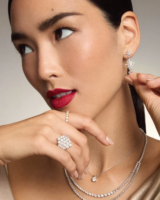Close-up of a beautiful Asian woman with red lipstick, adorned with diamond earrings, necklaces, and rings against a soft background.