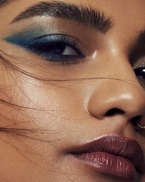 Close-up portrait of a woman with vibrant blue eyeshadow and glossy lips, highlighting beauty and makeup artistry in a studio setting.