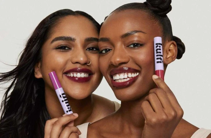 Two smiling women holding cosmetic tubes against a plain light background in a beauty portrait photograph by Nick Eucker.