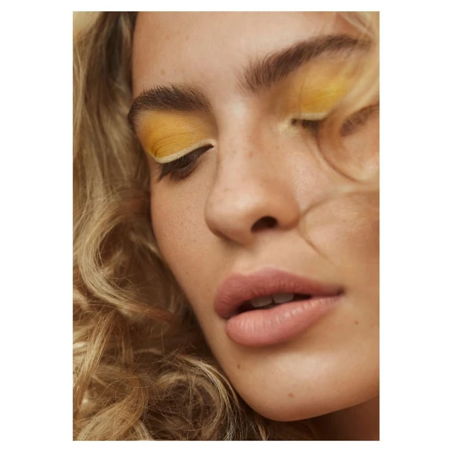 Close-up portrait of a woman with blonde curly hair and yellow eyeshadow, focusing on beauty and cosmetic elements in a studio setting.