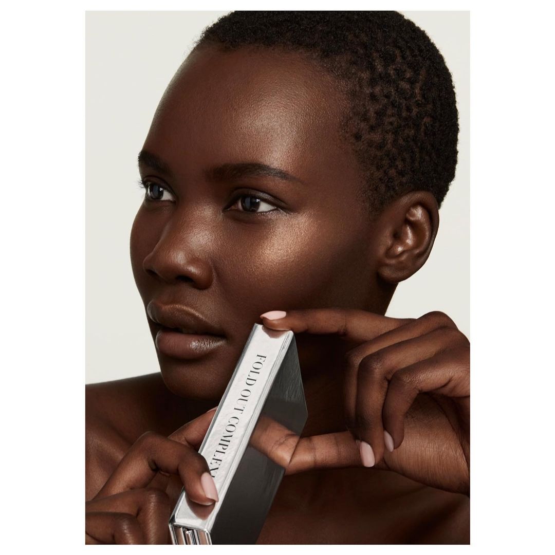 Close-up studio shot of a Black woman with short hair holding a silver cosmetic box, showcasing beauty and skincare.