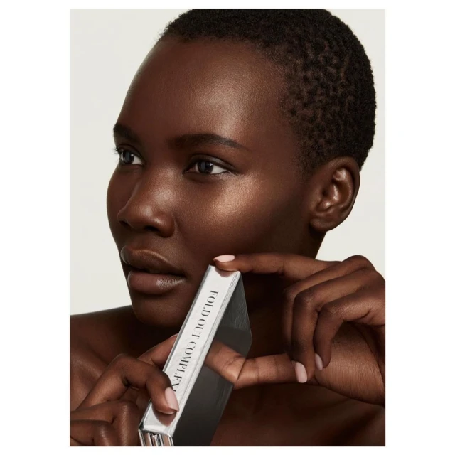 Close-up studio shot of a Black woman with short hair holding a silver cosmetic box, showcasing beauty and skincare.
