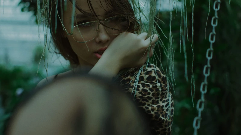 Close-up portrait of a woman wearing glasses and a leopard print top behind hanging vines in Brno, directed by Kateryna Petrykina.
