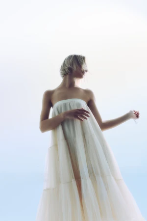 Low-angle shot of a woman in a strapless tiered off-white gown posing against a bright, luminous backdrop.