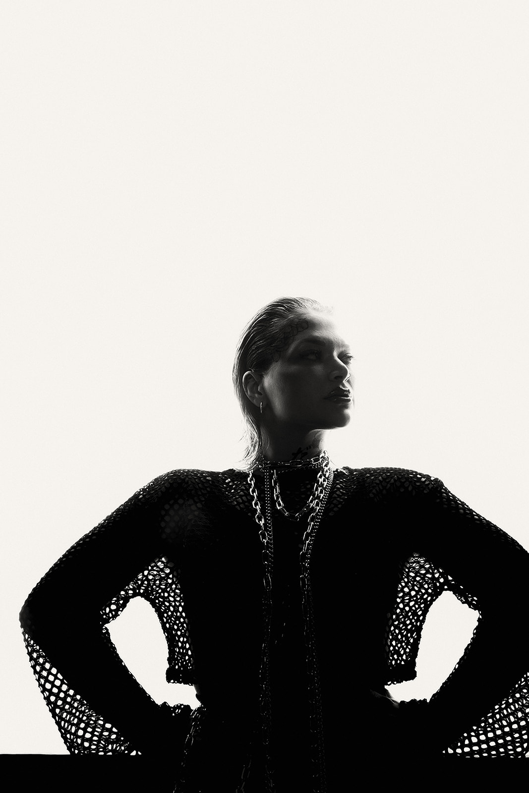 Silhouette of a woman with slicked-back hair wearing a dark mesh top against a bright white background.