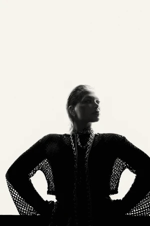 Silhouette of a woman with slicked-back hair wearing a dark mesh top against a bright white background.