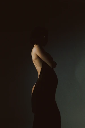 Profile silhouette of a pregnant woman wearing a dark dress against a low-key background captured by Kateryna Petrykina.