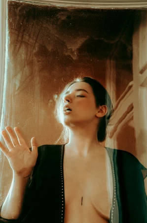 Woman in dark open robe with hand raised near an aged textured wall by Kateryna Petrykina