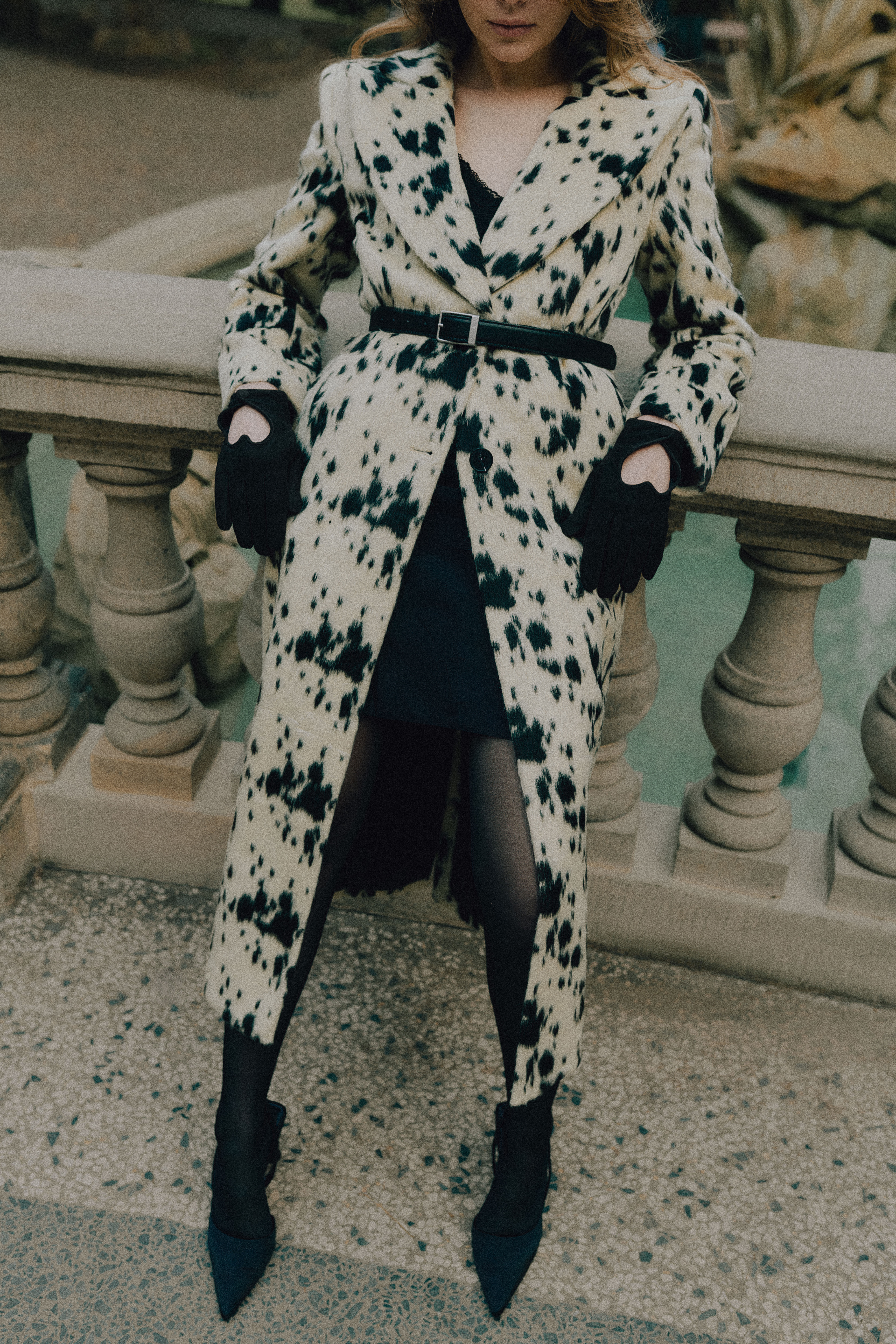 Woman in a cow-print patterned coat leaning against a stone balustrade outdoors in Brno.