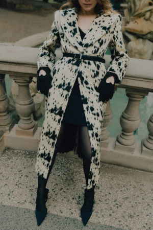 Woman in a cow-print patterned coat leaning against a stone balustrade outdoors in Brno.