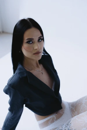 Portrait of a woman with dark hair wearing a black jacket and white lace tights against a plain white background