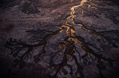 Aerial view of branching river channels cutting through a dark textured landscape with warm highlights