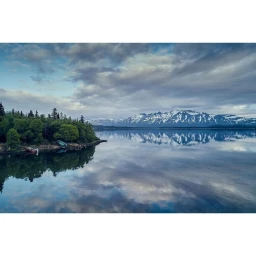 Tranquil mountain landscape with snow-capped peaks reflected in a calm lake under a cloudy sky captured by Nick Hall.