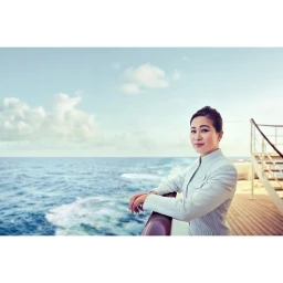 A woman leaning on a ship railing looking at the ocean under a clear sky, photographed by Nick Hall.