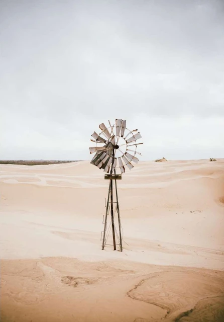 Windmill stands tall in the desert against a cloudy sky, highlighting the weathered texture and stark landscape.