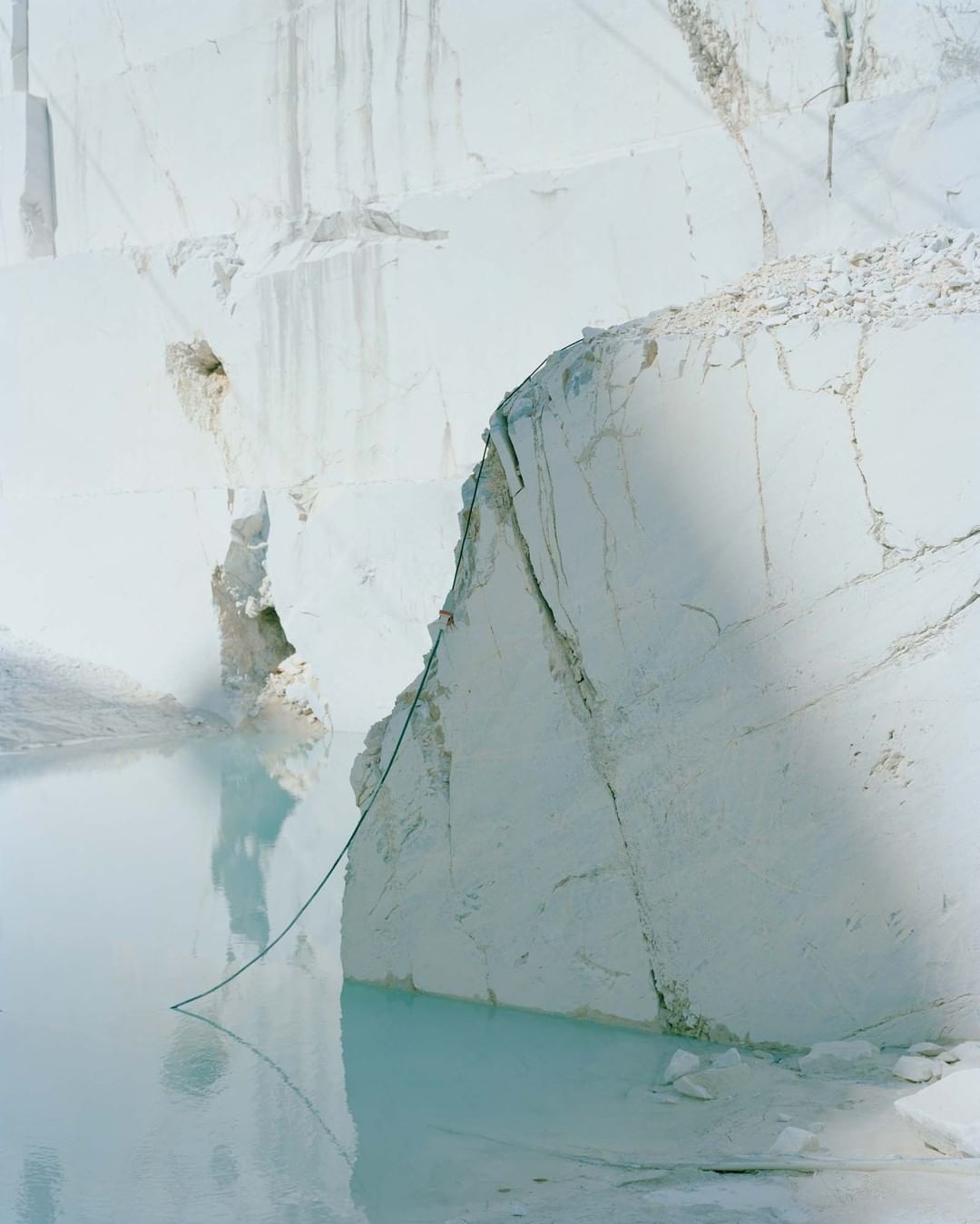 Dramatic view of a white marble quarry with pale blue water, showcasing textures, scale, and industrial extraction against a soft color palette.
