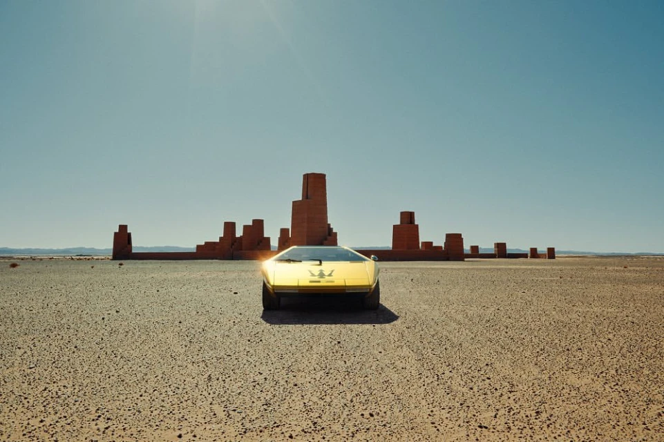 Yellow Maserati car parked in a desert landscape with red brick structures and a clear blue sky, captured in a wide shot.