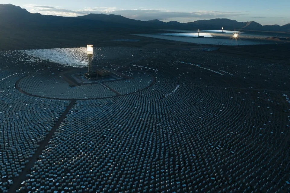 Vast solar power plant in desert landscape with rows of heliostat mirrors reflecting sunlight to central receiver towers, renewable energy.