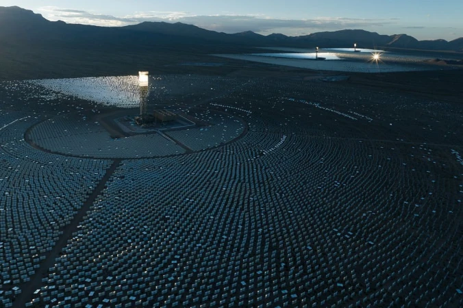 Vast solar power plant in desert landscape with rows of heliostat mirrors reflecting sunlight to central receiver towers, renewable energy.