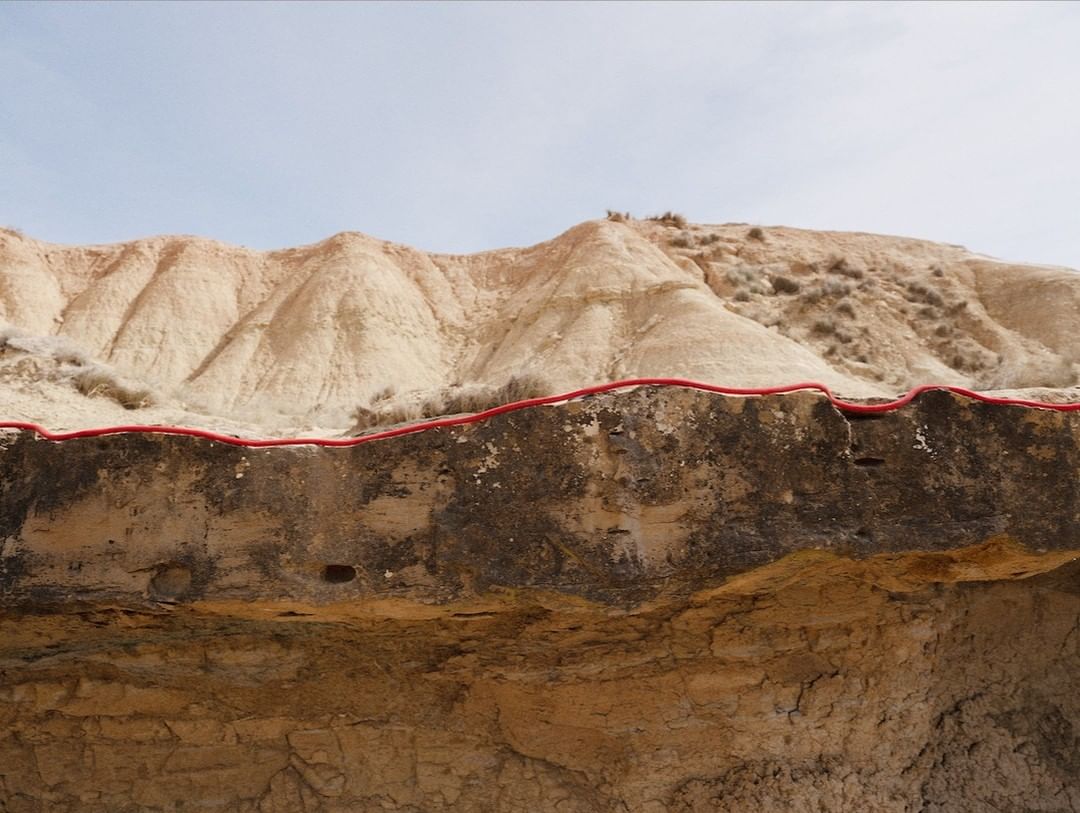 Eroded badlands landscape featuring soil stratification and textured sandstone formations against a bright, slightly overcast sky.