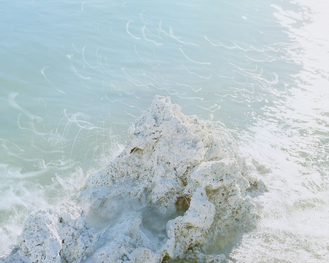 Close-up of turquoise ocean water washing over light-colored, textured rocks, creating a dreamy, serene waterscape scene. 
