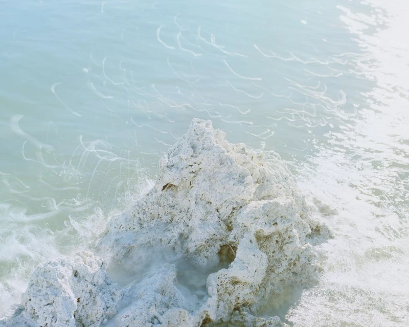 Close-up of turquoise ocean water washing over light-colored, textured rocks, creating a dreamy, serene waterscape scene. 