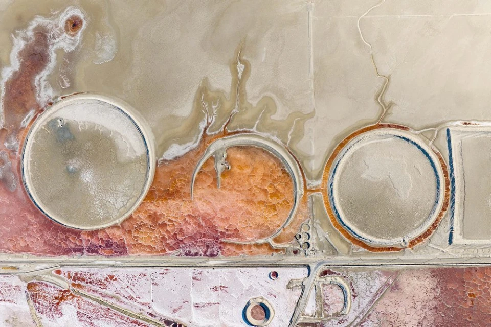 Aerial landscape with salt ponds featuring circular shapes, textured ground, and distinctive color variations including pink, white, and beige.