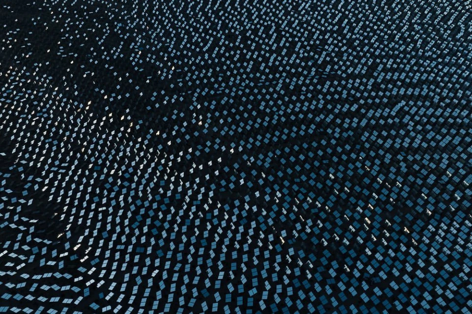 High-angle view of a solar panel field with many square panels, creating a patterned landscape of blues and dark hues.