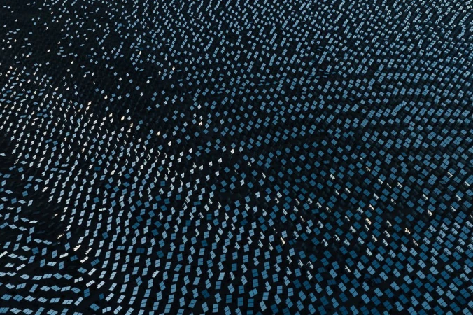 High-angle view of a solar panel field with many square panels, creating a patterned landscape of blues and dark hues.