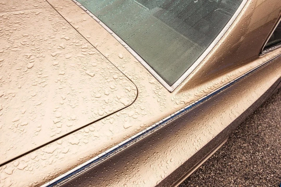 Close-up of a gold-toned classic car's rear with water droplets, showcasing vintage automotive design and reflections on a wet surface.