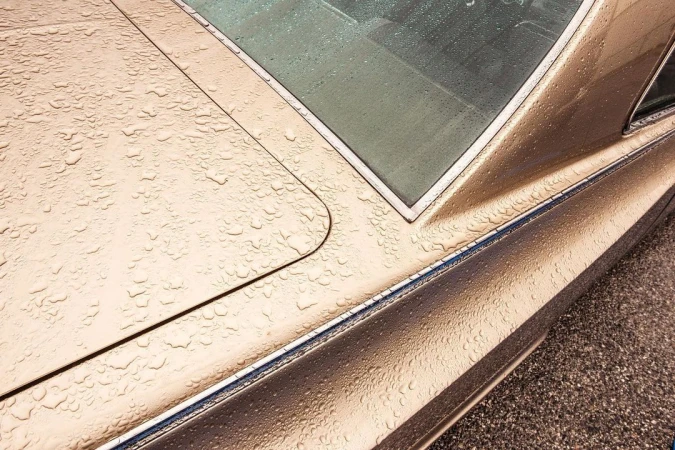 Close-up of a gold-toned classic car's rear with water droplets, showcasing vintage automotive design and reflections on a wet surface.