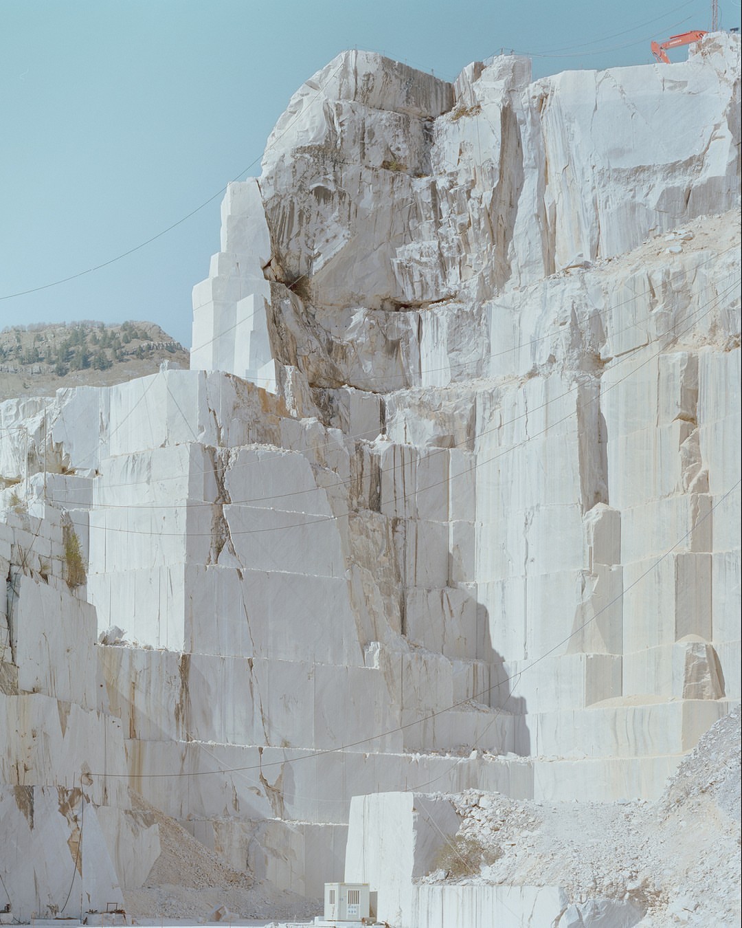 Large, terraced marble quarry with layered rock formations under a bright blue sky, showcasing industrial landscape and extraction.