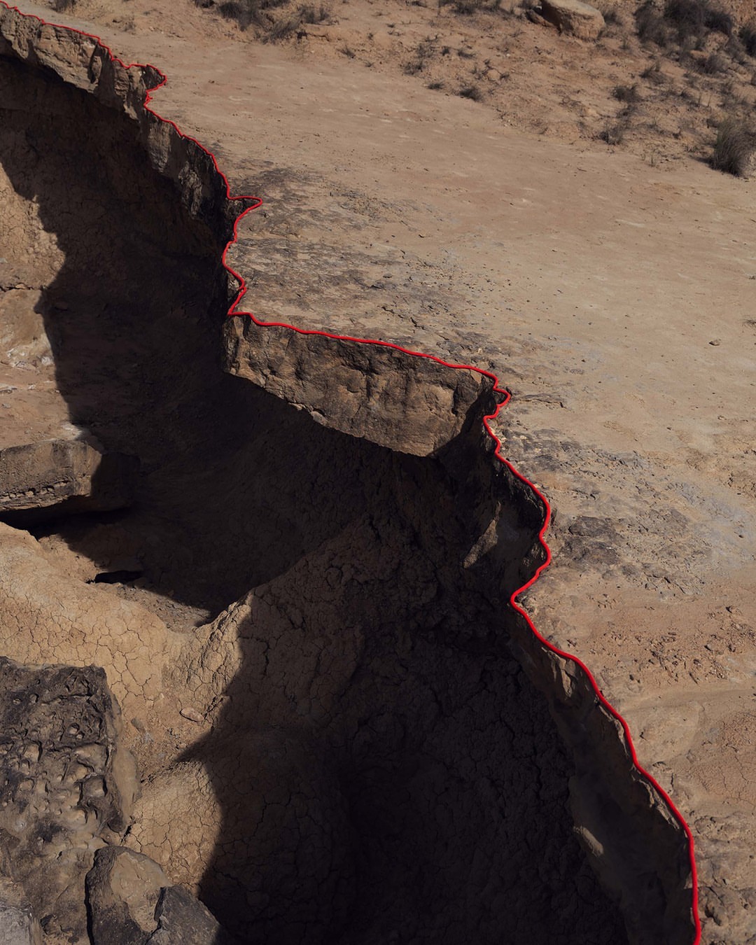 Aerial view of a rugged, arid landscape with a deep ravine or canyon cutting through the terrain, creating a dramatic geological formation.