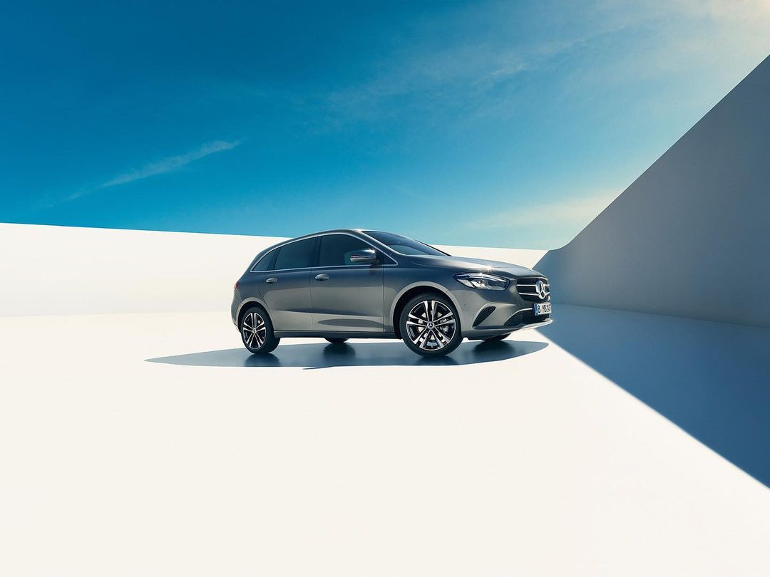 Sleek gray hatchback car parked on a white surface under a bright blue sky with wispy clouds, automotive photography.