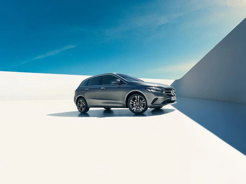 Sleek gray hatchback car parked on a white surface under a bright blue sky with wispy clouds, automotive photography.