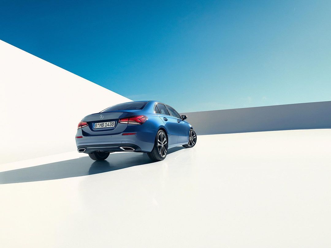 Rear view of a blue Mercedes-Benz A-Class sedan parked against a bright white wall and a clear blue sky with copy space.