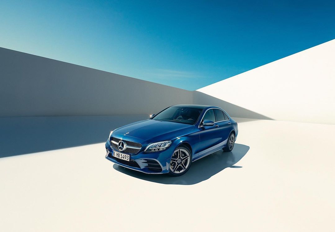 A blue Mercedes-Benz sedan sits angled on a white surface under a blue sky with white walls in the background, automotive perfection.