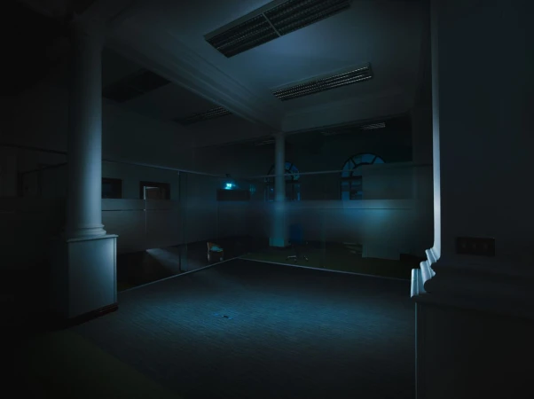 Interior shot of a large, dimly lit room with pillars, windows, and tiled floor, conveying a quiet, architectural space.