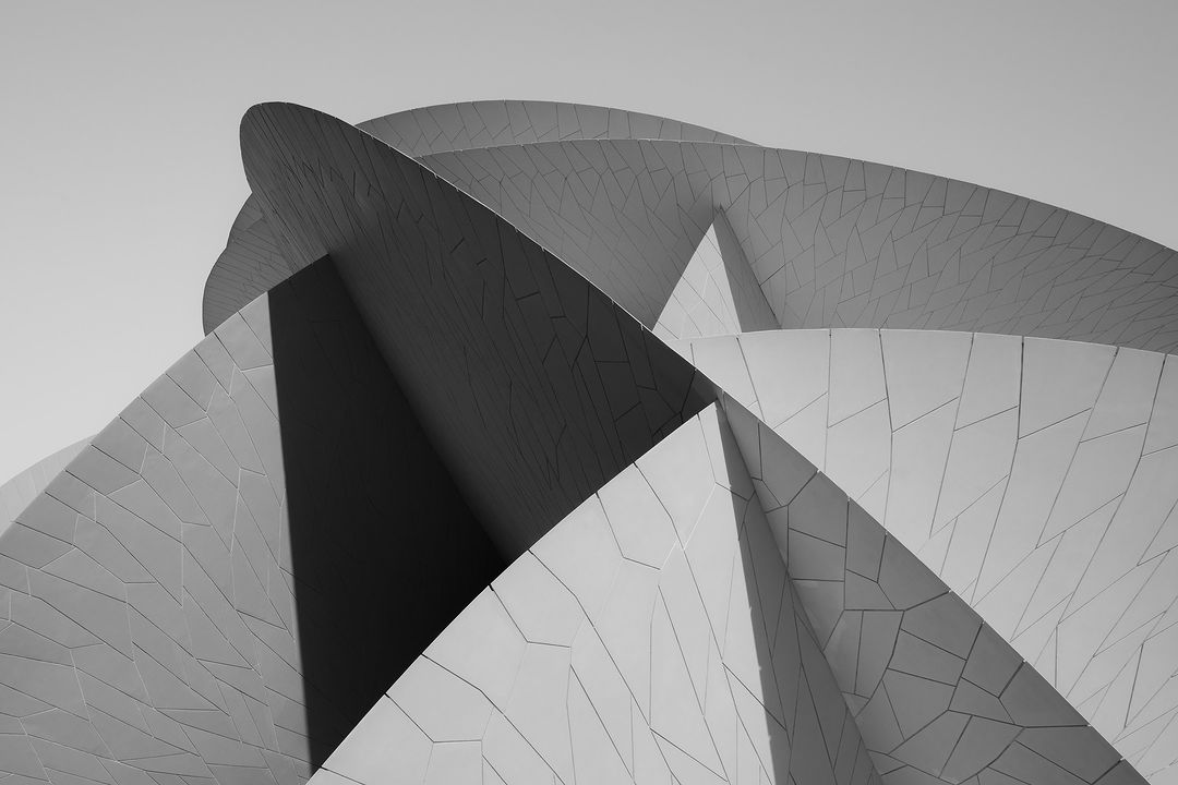Monochrome architectural view of the National Museum of Qatar featuring repeating curved geometric shapes, patterns, and stark shadows.