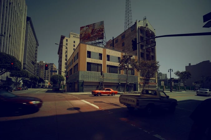 Urban streetscape with vintage red car, pickup truck on city streets amid buildings under a clear sky, capturing a classic Americana vibe.